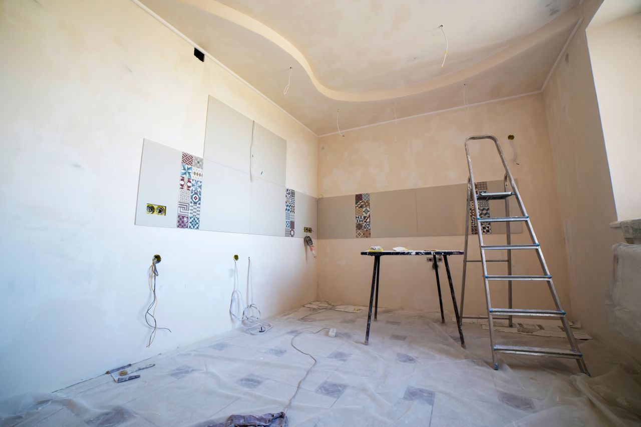 Interior view of a room under renovation with paint, tiles, and tools