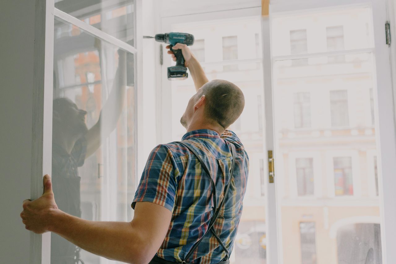Man installing window indoors with a drill, focusing on home renovation