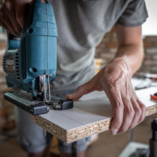 male carpenter cuts a wood with an electric jigsaw, working with a tree.